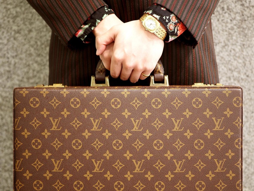 A model in a Takeo Kikuchi suit holds a Louis Vuitton suitcase.